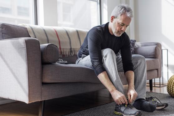 A man sitting on a couch and tying his shoelace